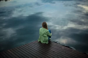 Woman sitting on edge of pier near lake